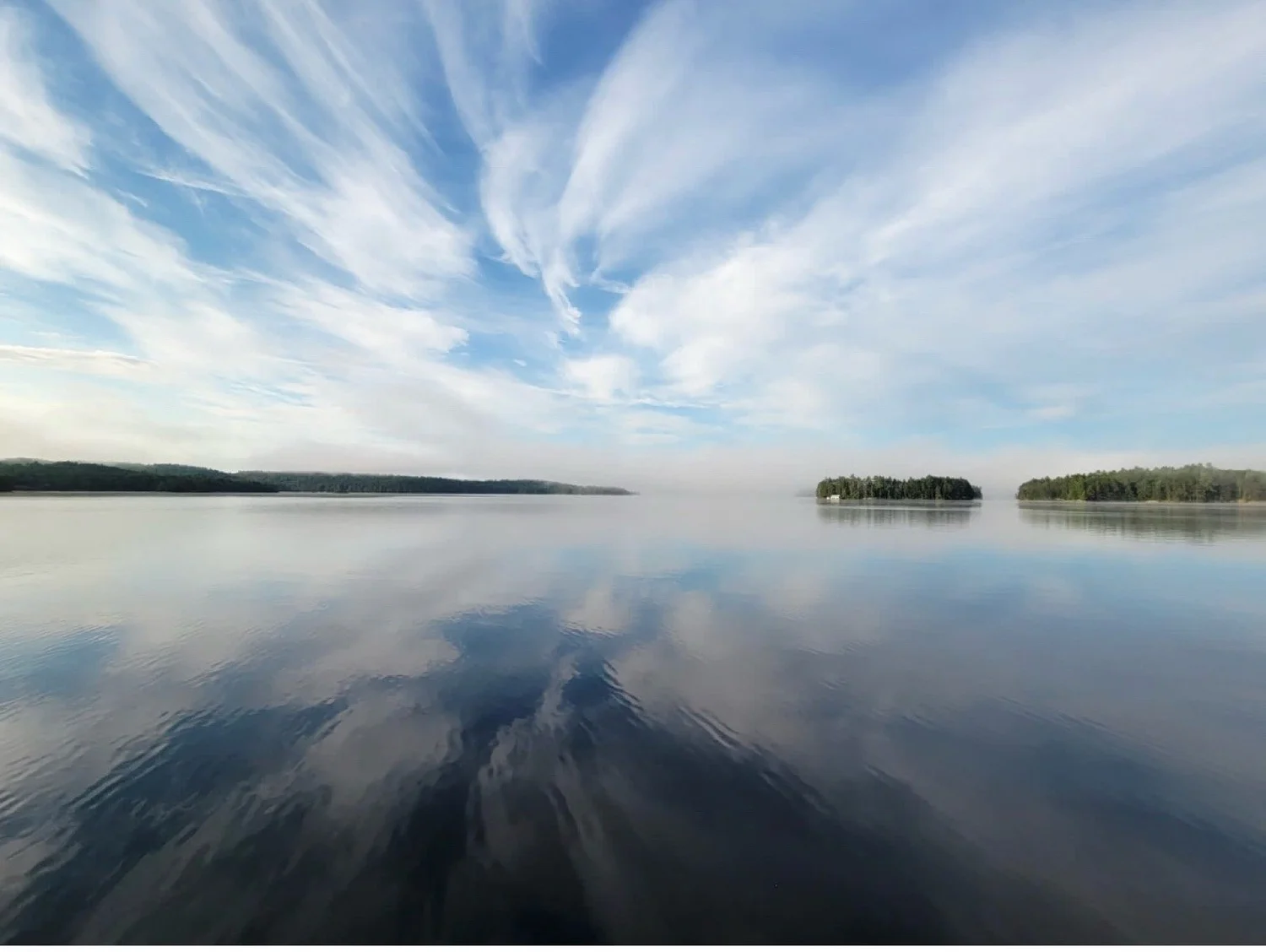 A calm lake with the sky and clouds opening up in the reflection.
