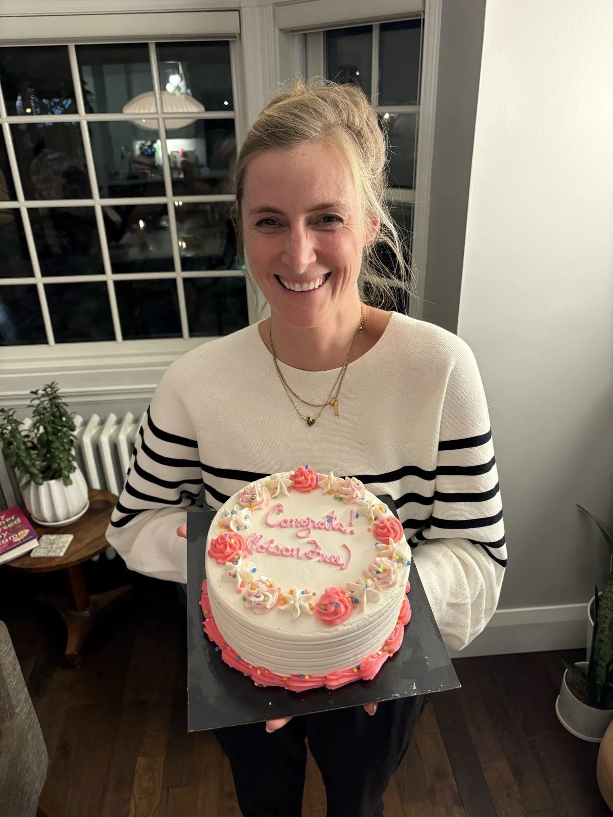 Carly holding a cake iced with “Congrats! (Poison Free.)”